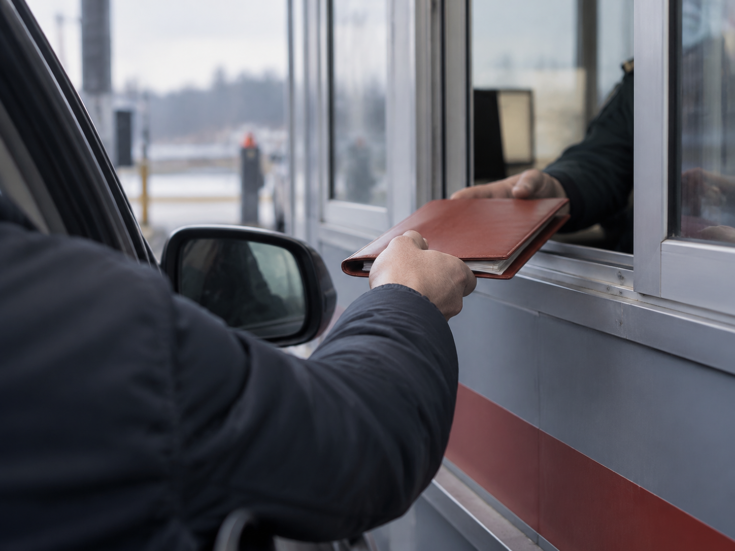Osobné auto zastavené pri kontrolnej búdke, vodič podáva doklady